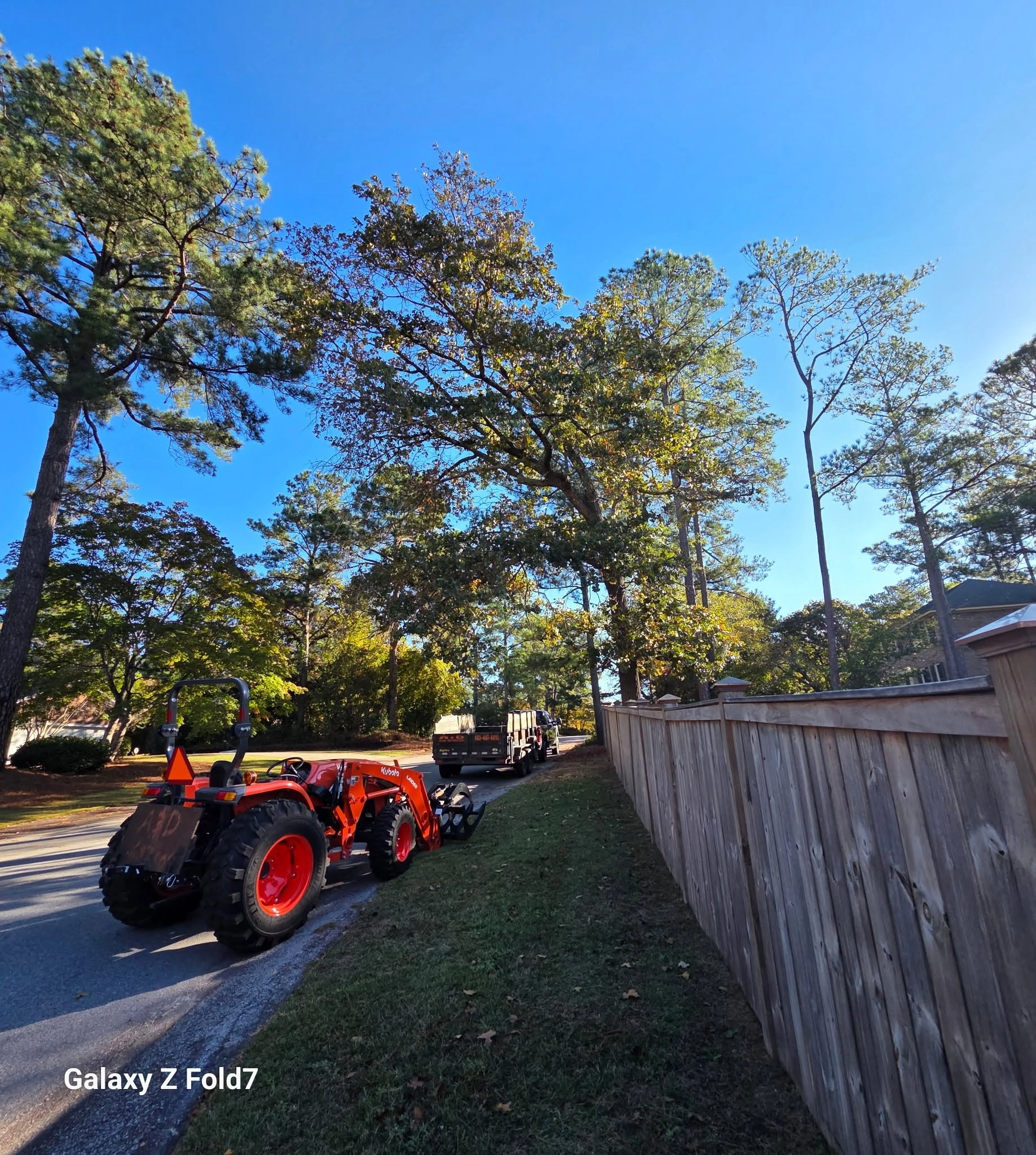 Orange kubota tractor grapple roadside wood privacy fence ta