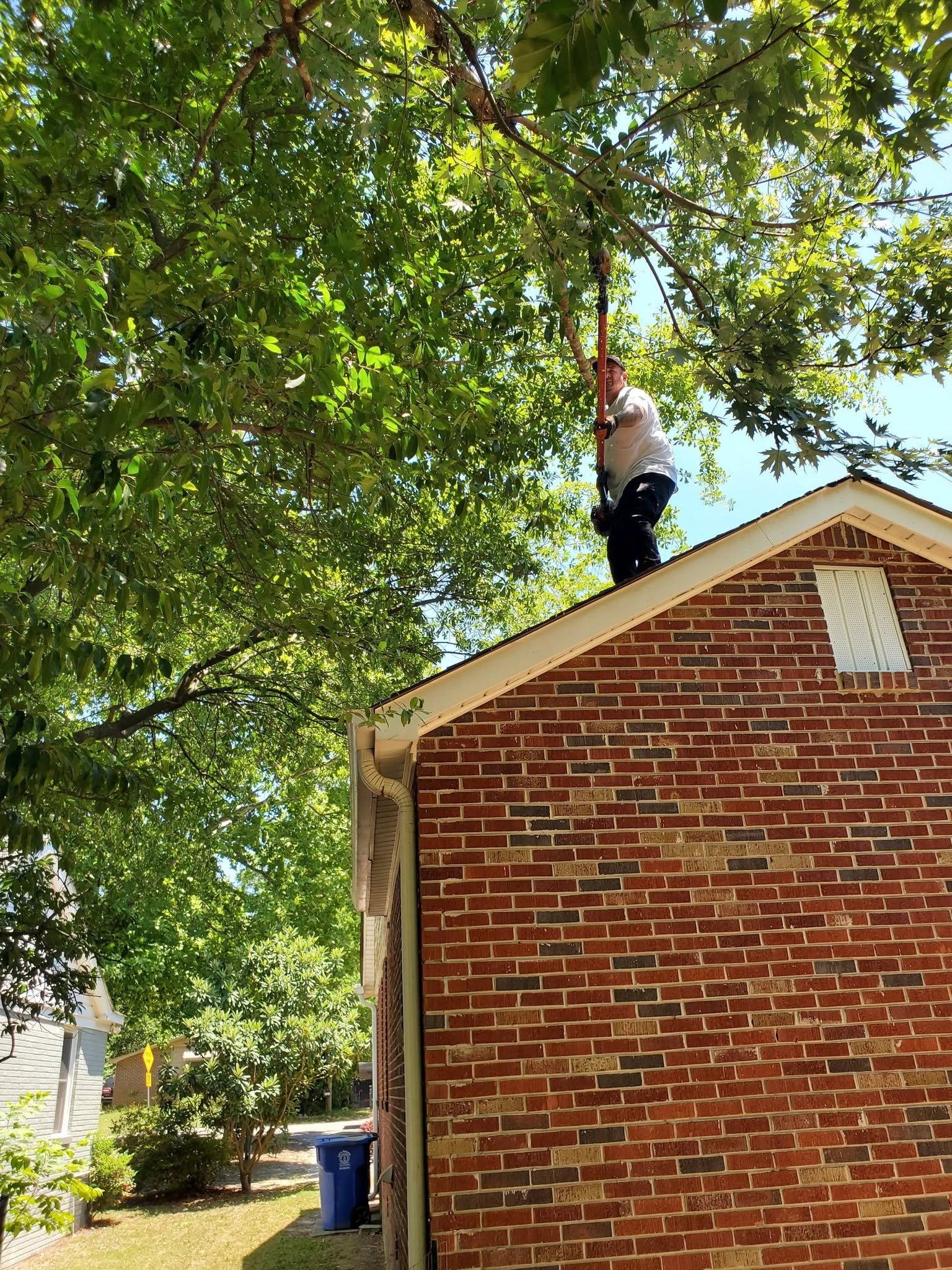 Worker on brick gable roof pole saw oak limbs cayce sc