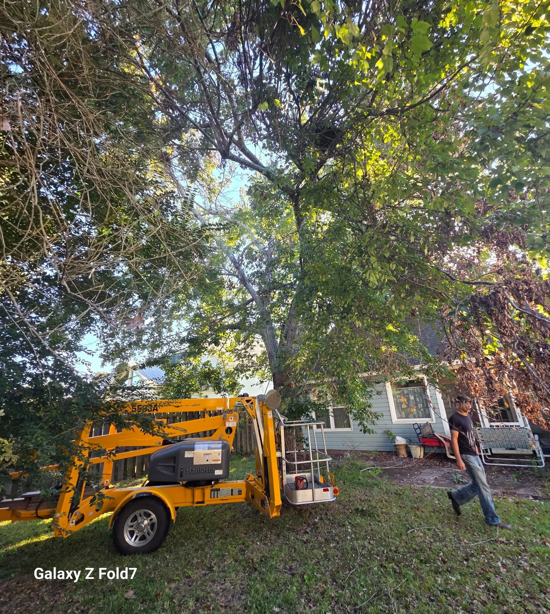 Yellow haulotte towable lift blue siding house backyard work