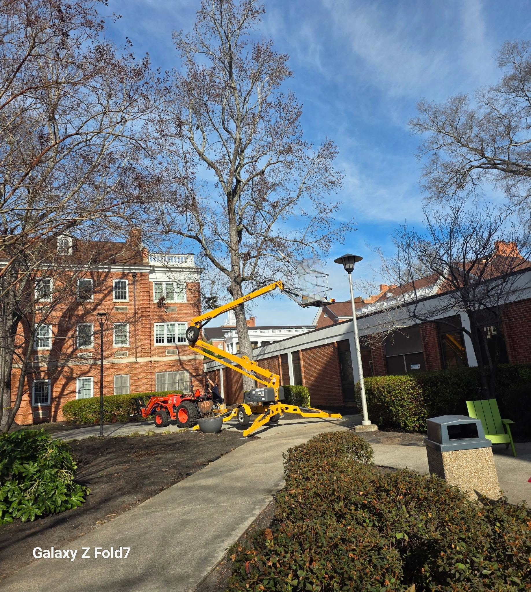 Yellow towable boom lift bare oak brick campus courtyard wal